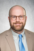Photo of Kyle Flippo in tan suit jacket and blue tie
