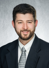 Photo of Joshua Tatz in dark suit jacket and grey tie